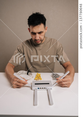 Vertical portrait of technician male examining a wireless router and ethernet cables on a white table, focusing on internet setup and network configuration tasks, ensuring reliable connectivity. 137780648