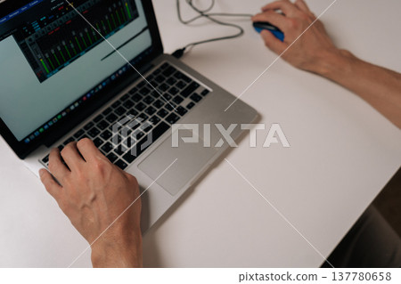 Close-up of person working on laptop computer with wired mouse, typing on keyboard and navigating digital audio workstation interface, concept of remote work, digital production, ttechnology skills. Close-up of person working on laptop computer with wired mouse, typing on keyboard and navigating digital audio workstation interface, concept of remote work, digital production, ttechnology skills. 137780658