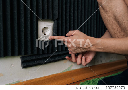 Male hand pointing at electrical socket recess engineered into a soundproof acoustic foam panel during home studio soundproofing installation or noise reduction treatment. Male hand pointing at electrical socket recess engineered into a soundproof acoustic foam panel during home studio soundproofing installation or noise reduction treatment. 137780673