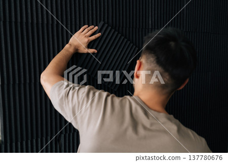 Man installing acoustic foam panels on a wall, enhancing a private studio for soundproofing and sound absorption, building a quiet space for music creation and audio engineering. Man installing acoustic foam panels on a wall, enhancing a private studio for soundproofing and sound absorption, building a quiet space for music creation and audio engineering. 137780676