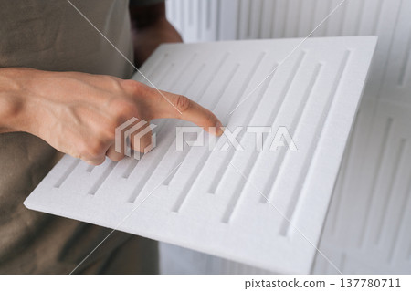 Closeup hand of professional touching white acoustic foam panel with pattern, preparing for installation to absorb sound and improve room acoustics in recording studio or quiet space. 137780711