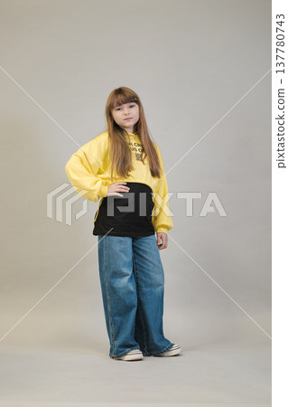 Posing with her hands on her hips, a girl in a black t-shirt and wide-leg jeans stands confidently against a neutral background. This image reflects the modern trend of combining casual style with a Posing with her hands on her hips, a girl in a black t-shirt and wide-leg jeans stands confidently against a neutral background. This image reflects the modern trend of combining casual style with a 137780743