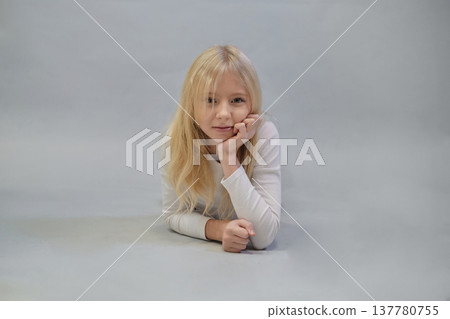 Dressed in a white crop top and plaid skirt, a girl with blonde hair poses with her hands on her hips, exuding confidence against a simple backdrop. This photo captures modern, youthful style and a 137780755