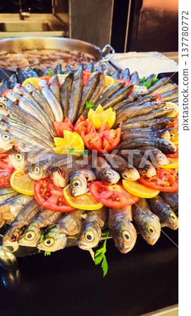 Large platter of fresh fish arranged radially with lemon wedges and tomatoes in a restaurant kitchen. The appetizing seafood composition represents gastronomy, buffet dining and fresh seafood 137780772