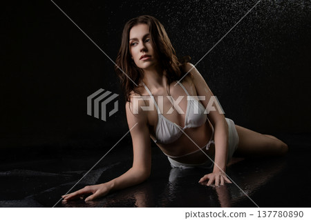 Dramatic studio portrait of a woman in a white bikini lying in water on a black background. Dramatic studio portrait of a woman in a white bikini lying in water on a black background. 137780890