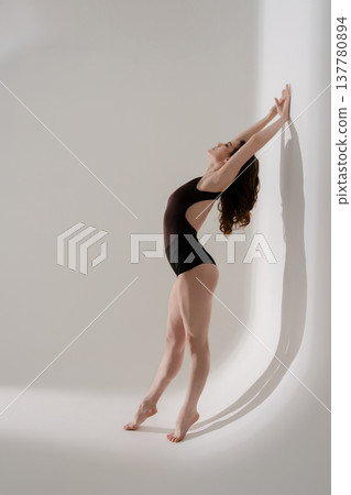 Elegant female dancer in leotard arching back in a minimalist studio. Elegant female dancer in leotard arching back in a minimalist studio. 137780894
