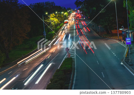 Night city road with long exposure light trails, vehicles moving along urban street, traffic flow, transportation activity, illuminated metropolitan. Blurred urban mobility traffic movement Night city road with long exposure light trails, vehicles moving along urban street, traffic flow, transportation activity, illuminated metropolitan. Blurred urban mobility traffic movement 137780903