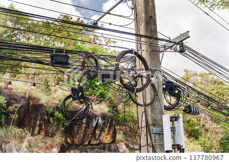 Messy overhead utility cables and telecom wires on concrete pole in tropical Thailand Messy overhead utility cables and telecom wires on concrete pole in tropical Thailand 137780967