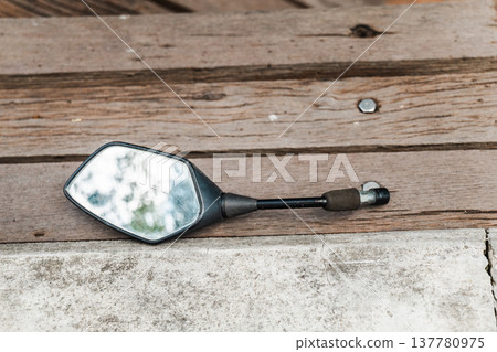 Broken scooter rearview mirror lying on wooden surface concept of road accident Broken scooter rearview mirror lying on wooden surface concept of road accident 137780975