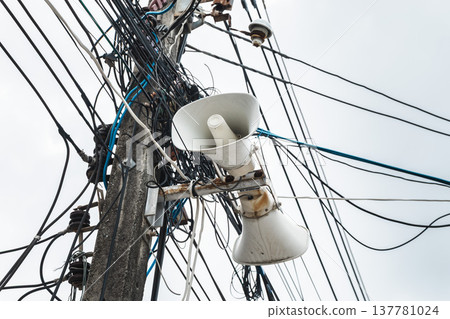 Loudspeaker mounted on utility pole with tangled electrical wires in Thailand 137781024