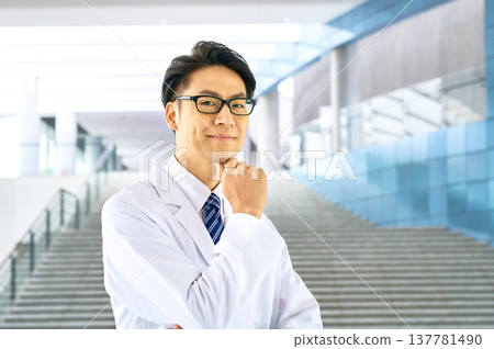 A young male doctor smiles gently at the camera. Trustworthy, reassuring, medical consultation, doctor in a white coat, portrait. A young male doctor smiles gently at the camera. Trustworthy, reassuring, medical consultation, doctor in a white coat, portrait. 137781490