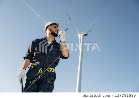 Using walkie talkie. Engineer in field checking on wind turbine production Using walkie talkie. Engineer in field checking on wind turbine production 137781689