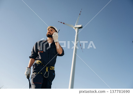 Speaking by walkie talkie. Engineer in field checking on wind turbine production Speaking by walkie talkie. Engineer in field checking on wind turbine production 137781690