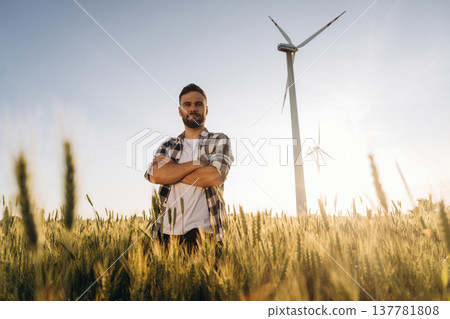 Guy engineer in wheat field against wind turbines Guy engineer in wheat field against wind turbines 137781808