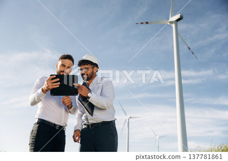 Getting to know the plan. Two men engineers are on field, with wind turbines 137781861