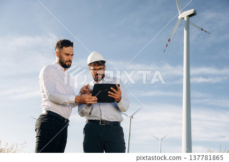 Getting to know the plan. Two men engineers are on field, with wind turbines Getting to know the plan. Two men engineers are on field, with wind turbines 137781865