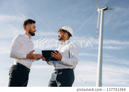 Two men engineers are on field, with wind turbines Two men engineers are on field, with wind turbines 137781866