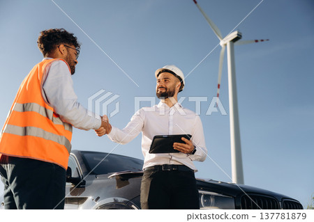 Two men engineers are on field, with wind turbines Two men engineers are on field, with wind turbines 137781879