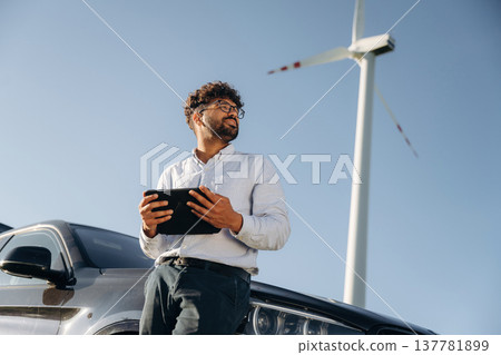 Male engineer in field checking on wind turbine production Male engineer in field checking on wind turbine production 137781899