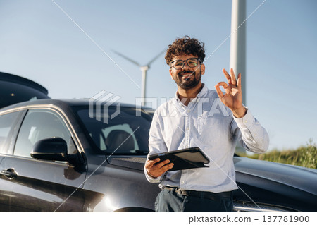 Smiling, positive facial expression. Male engineer in field checking on wind turbine production 137781900