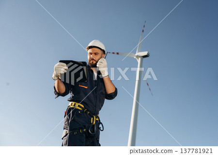 Speaking by walkie talkie. Engineer in field checking on wind turbine production Speaking by walkie talkie. Engineer in field checking on wind turbine production 137781921
