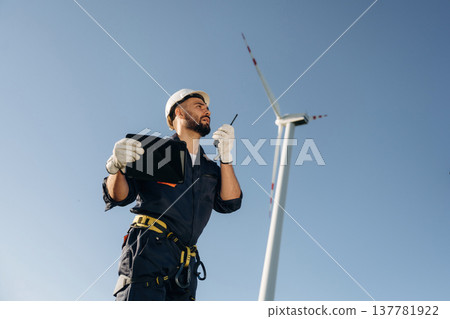 Speaking by walkie talkie. Engineer in field checking on wind turbine production 137781922