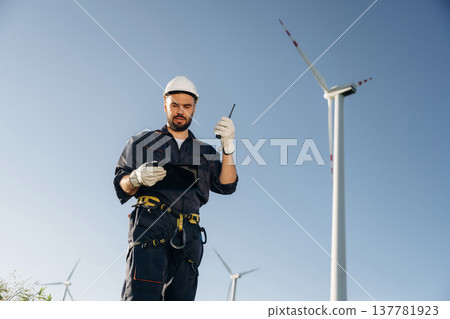 Giving orders by using walkie talkie. Engineer in field checking on wind turbine production Giving orders by using walkie talkie. Engineer in field checking on wind turbine production 137781923