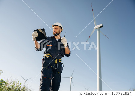 Giving orders by using walkie talkie. Engineer in field checking on wind turbine production Giving orders by using walkie talkie. Engineer in field checking on wind turbine production 137781924