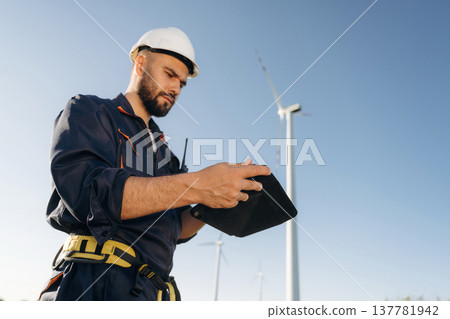 Reading information on digital tablet. Engineer in field checking on wind turbine production 137781942