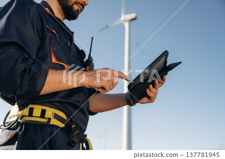 Detailed close up view of engineer in field with wind turbines against him Detailed close up view of engineer in field with wind turbines against him 137781945