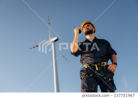 Technician is giving orders by walkie talkie. Engineer in field checking on wind turbine production 137781967