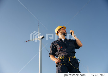 View from below, standing. Engineer in field checking on wind turbine production View from below, standing. Engineer in field checking on wind turbine production 137781968