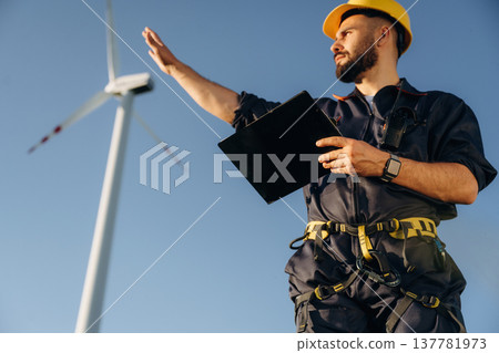 View from below, standing. Engineer in field checking on wind turbine production View from below, standing. Engineer in field checking on wind turbine production 137781973
