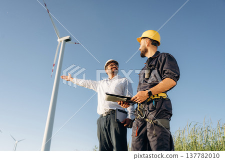 Making the business. Two men engineers are on field, with wind turbines 137782010