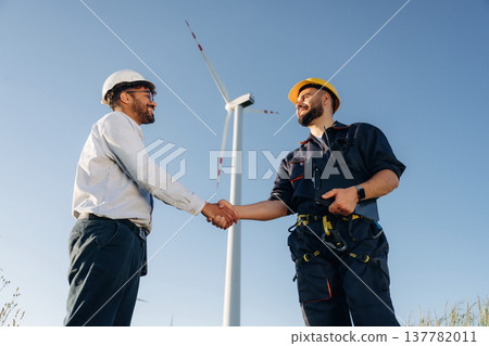 Greetings handshake. Nice deal. Two men engineers are in field, with wind turbines 137782011