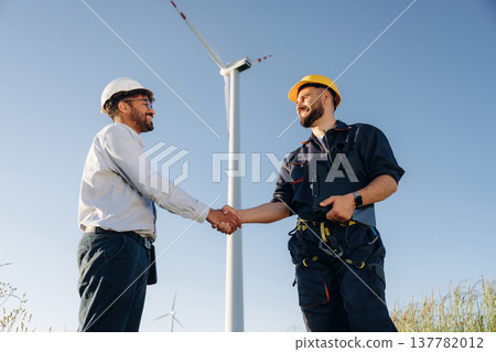 Greetings handshake. Nice deal. Two men engineers are in field, with wind turbines 137782012