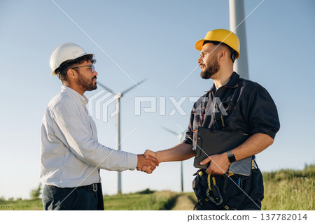 Greetings handshake. Nice deal. Two men engineers are in field, with wind turbines 137782014
