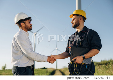 Greetings handshake. Nice deal. Two men engineers are in field, with wind turbines Greetings handshake. Nice deal. Two men engineers are in field, with wind turbines 137782015