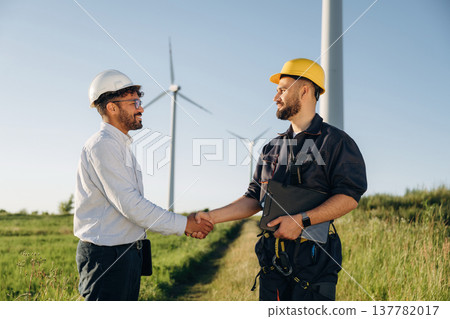 Cooperation concept. Two men engineers are on field, with wind turbines 137782017