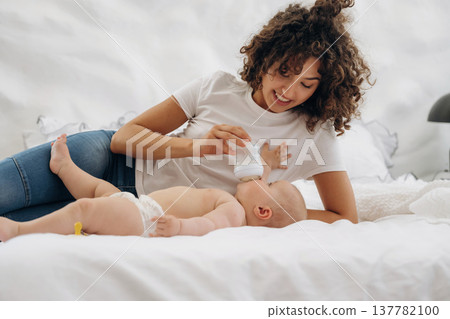 Feeding by using a bottle. Young woman is with her young baby daughter indoors 137782100