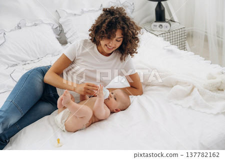 Giving food by using bottle. Young woman is with her young baby daughter indoors 137782162