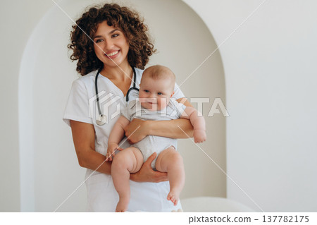 Smiling, holding baby in hands. Female doctor is with newborn indoors 137782175