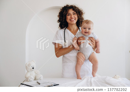 On the table and in hands, trying to stand up. Female doctor is with newborn baby indoors 137782202