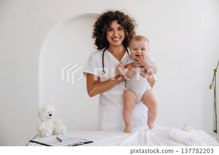 On the table and in hands, trying to stand up. Female doctor is with newborn baby indoors 137782203