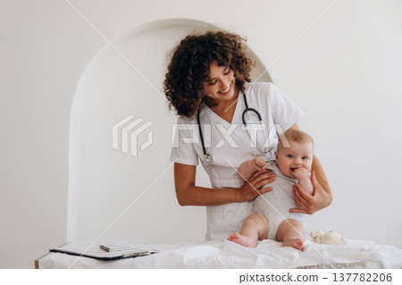 On the table and in hands, trying to stand up. Female doctor is with newborn baby indoors On the table and in hands, trying to stand up. Female doctor is with newborn baby indoors 137782206