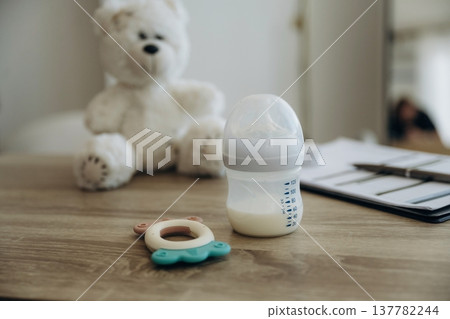 Baby bottle and teddy bear toy on the wooden table 137782244