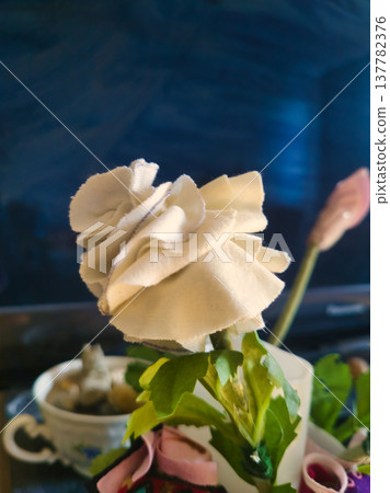 Macro View of Handmade White Fabric Rose with Layered Petals. Artisan Textile Floral Craft Detail for Sustainable Decor and DIY Inspiration. Close-up of Upcycled Cloth Blossom on Green Wired Stem. Macro View of Handmade White Fabric Rose with Layered Petals. Artisan Textile Floral Craft Detail for Sustainable Decor and DIY Inspiration. Close-up of Upcycled Cloth Blossom on Green Wired Stem. 137782376
