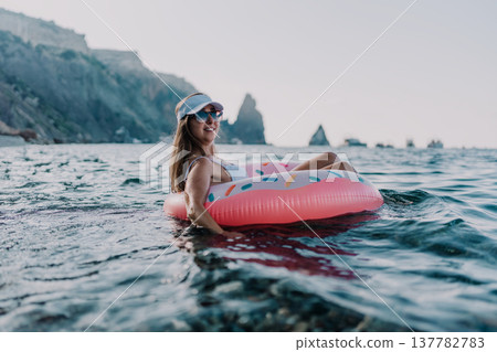 Woman, donut, ocean. Happy woman relaxing on inflatable donut in clear blue sea near rocky cliffs. Woman, donut, ocean. Happy woman relaxing on inflatable donut in clear blue sea near rocky cliffs. 137782783