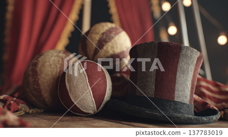 Vintage circus hat and balls on wooden table with red curtains and lights in background during a nighttime scene Vintage circus hat and balls on wooden table with red curtains and lights in background during a nighttime scene 137783019