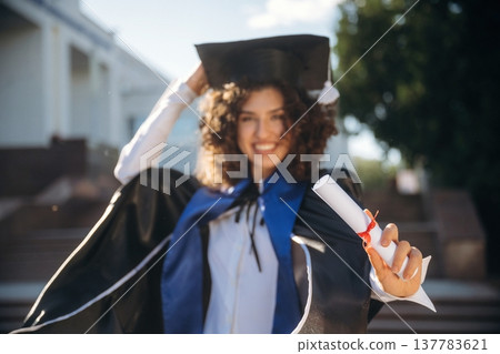 Finally finished, diploma in hand. Cheerful graduate student in a gown is standing outdoors Finally finished, diploma in hand. Cheerful graduate student in a gown is standing outdoors 137783621